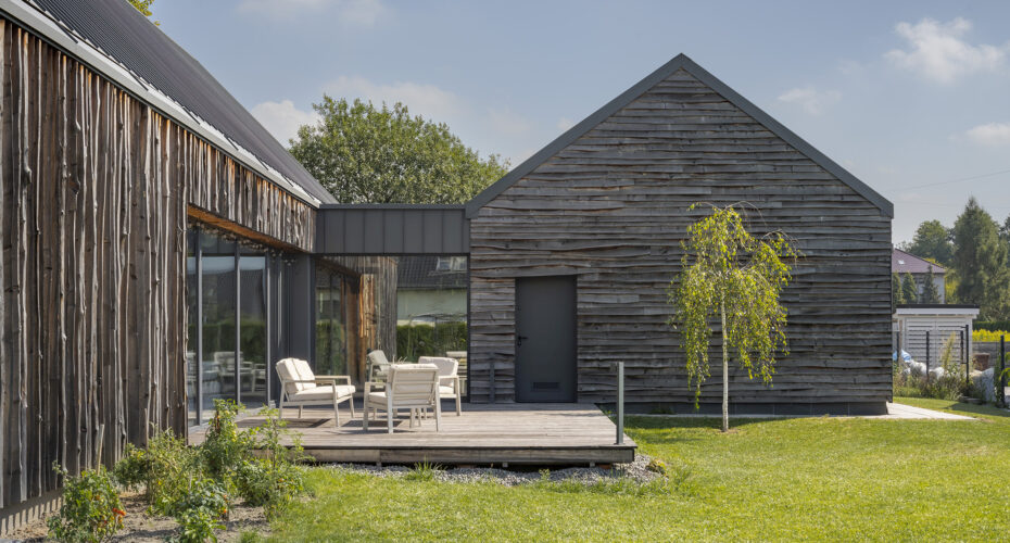 Widok z ogrodu na taras i dom z drewnianą nieheblowaną elewacją projektu