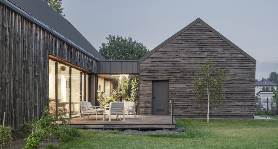 Widok z ogrodu na taras i dom z drewnianą nieheblowaną elewacją projektu