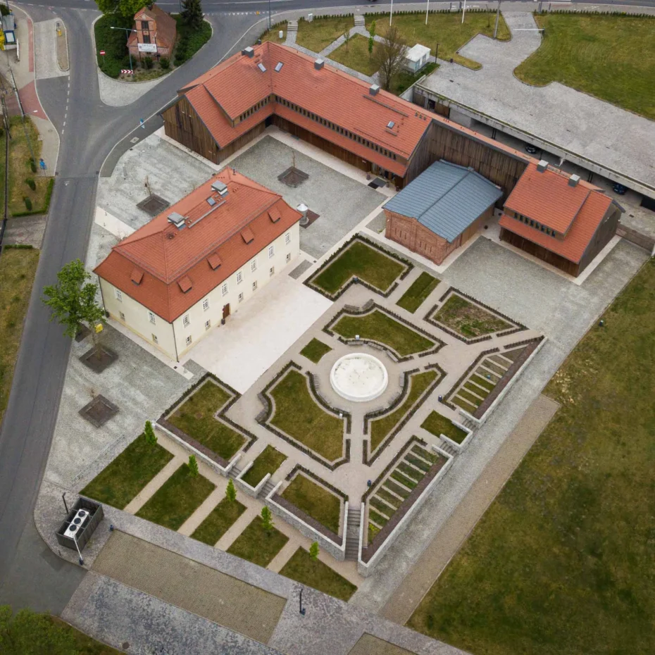 widok z lotu ptaka zabytkowego dworu z dachem z dachówki i towarzyszącą zabudową drewnianą