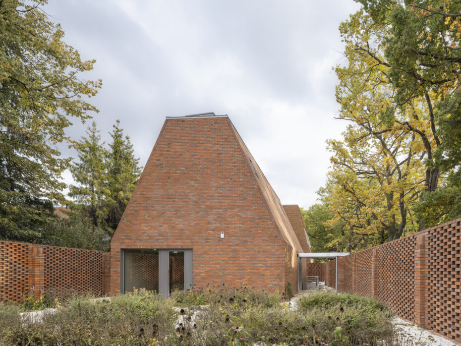 Ogród z widokiem na budynek z ceglaną elewacją i ażurowym ceglanym płotem.