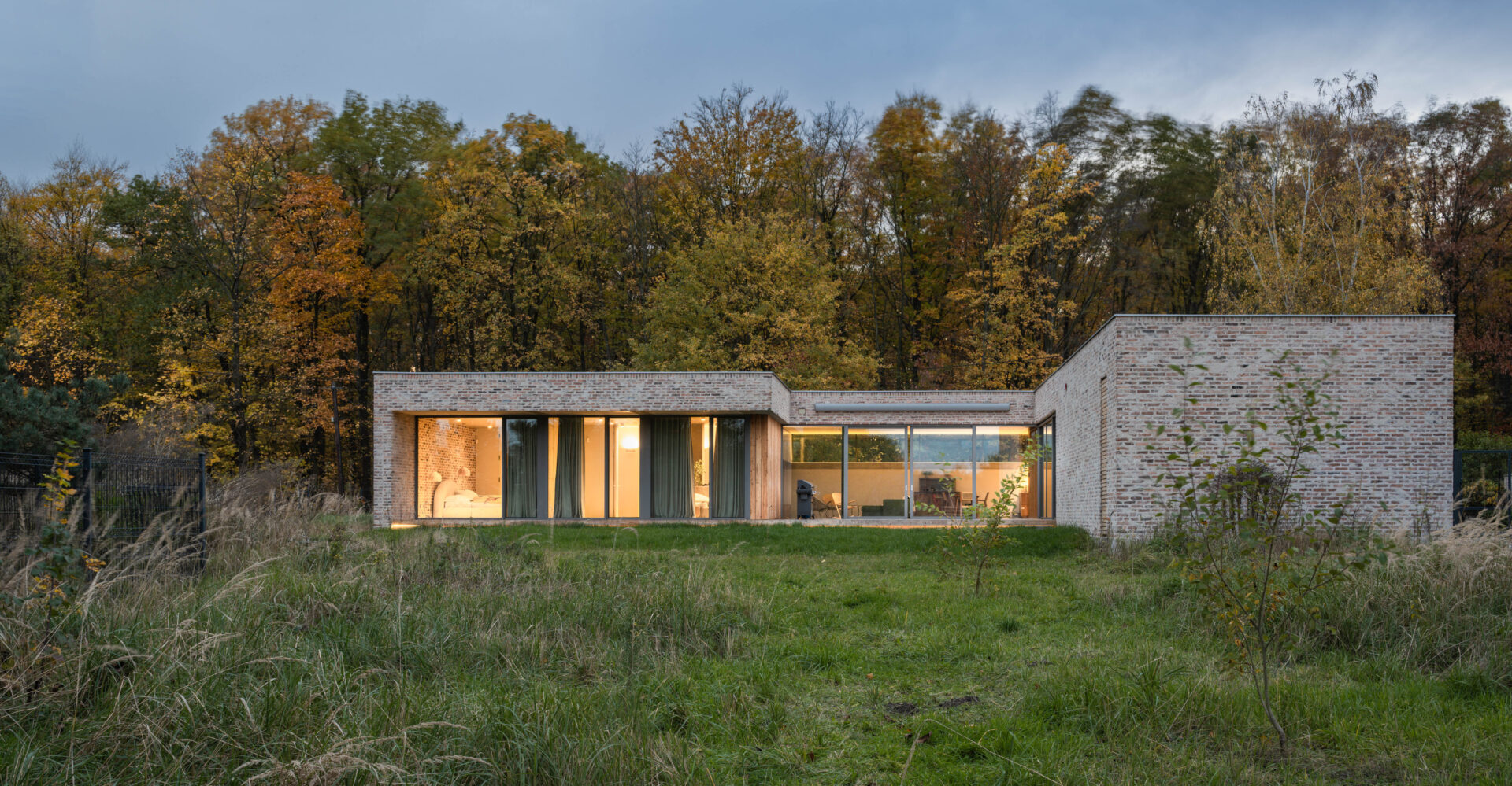 Dom jednorodzinny na skraju lasu po zmroku z rozświetlonymi wnętrzami