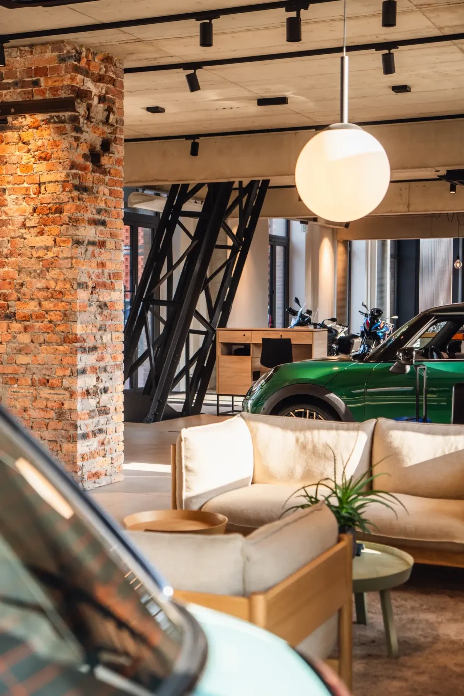 Auta marki MINI stojące w industrialnym wnętrzu zrewitalizowanego szybu kopalni Kleofas w Katowicach, na tle wysokich okien, czarnej metalowej konstrukcji oraz nowej betonowej zabudowy.